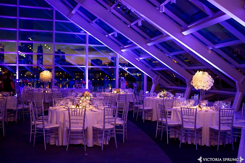 Tables And Chairs With Floral Centerpieces And A Purple Color Lighting