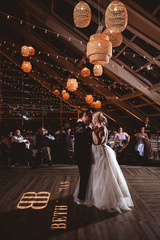 Groom And Bride Dancing Under The Rattan Chandeliers And String Lights