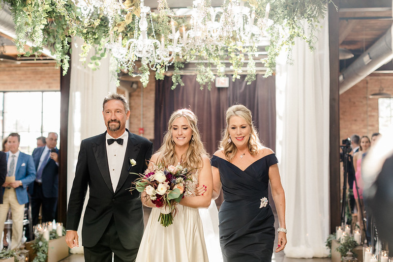 Bride With Her Parents Walking In The Aisle Under Chandelier