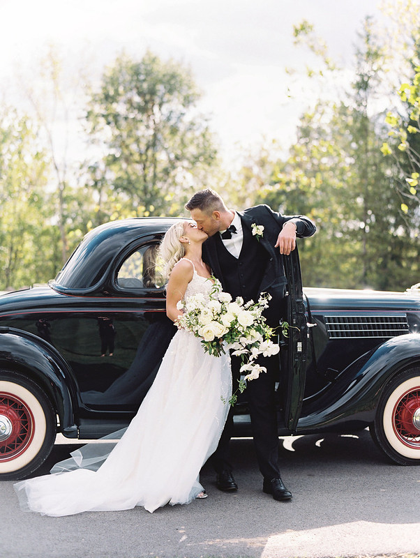 Bride And Groom Kissing On The Side Of The Black Classic Car