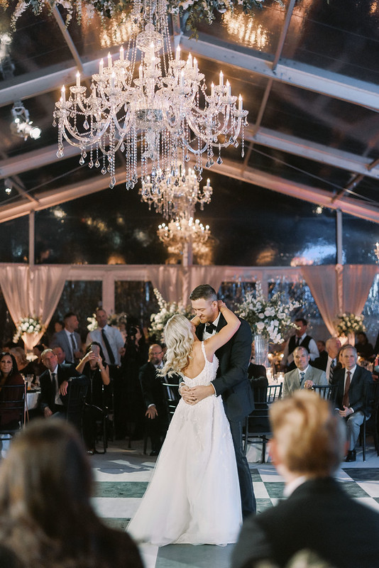 Bride And Groom Dancing In White And Black Checkered Dance Floor Under Wedding Chandeliers, Guest Watching Them