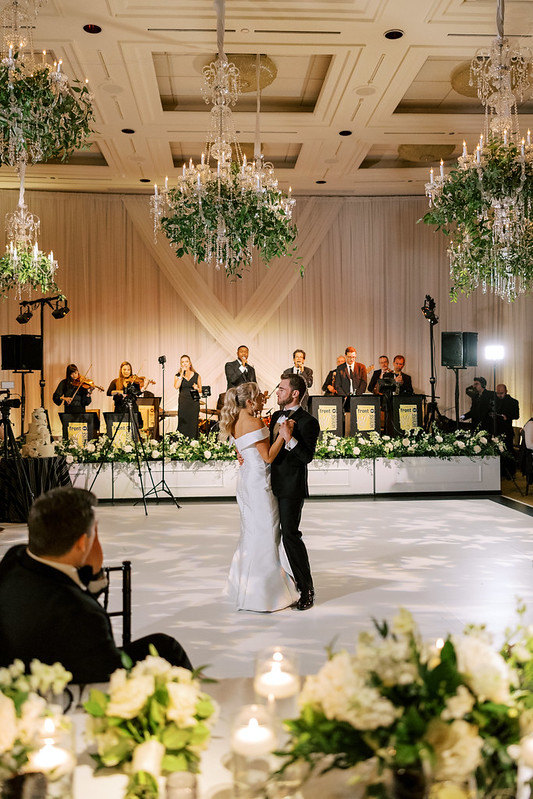 Bride And Groom Dancing Under The Crystal Wedding Chandeliers With Greenery