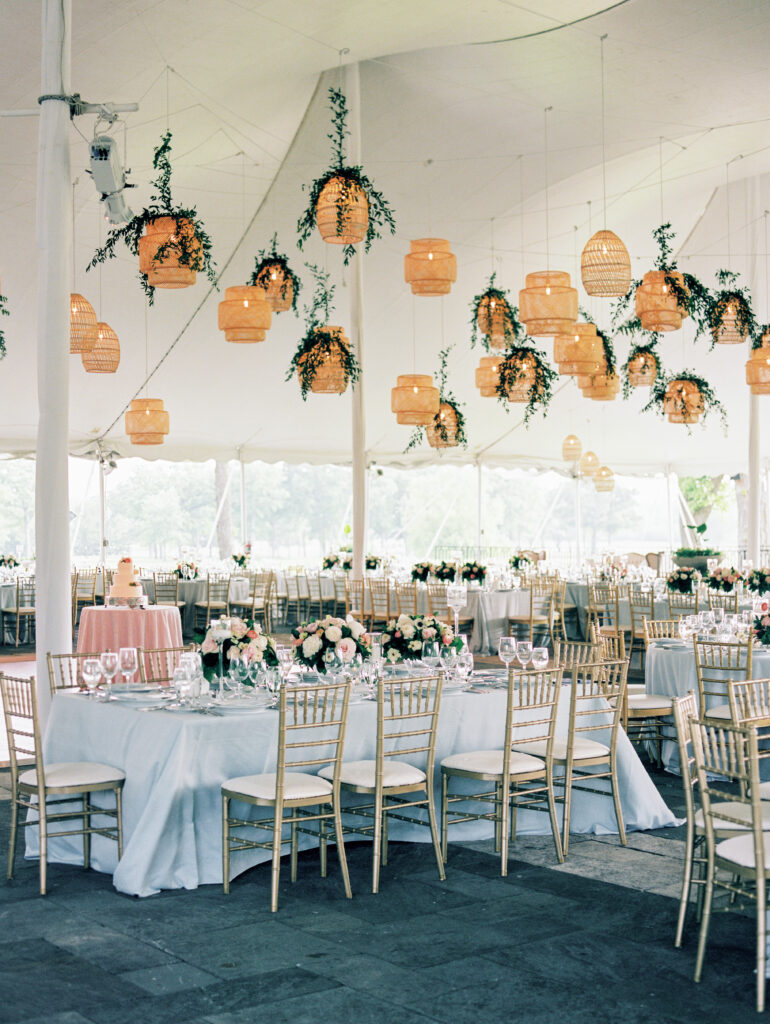 Under A White Tent, Tables And Golden Chairs Arrangement And Many Rattan Lantern Wedding Lighting Above