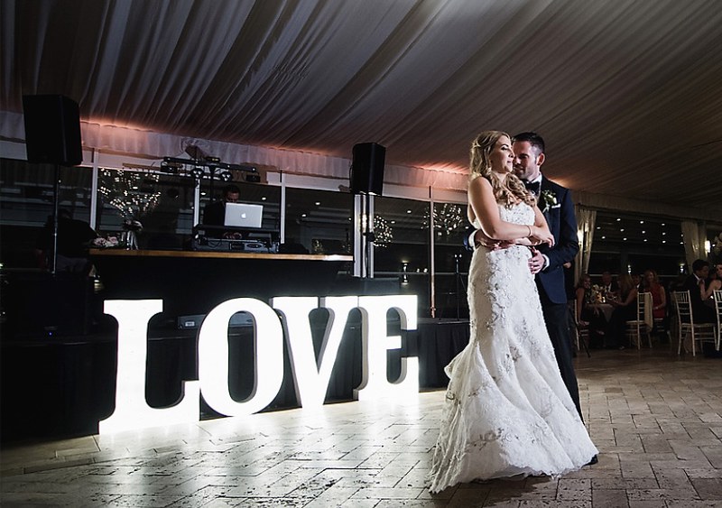 Bride And Groom Taking Picture With Marquee Letters Spell Out Love As Their Backdrop