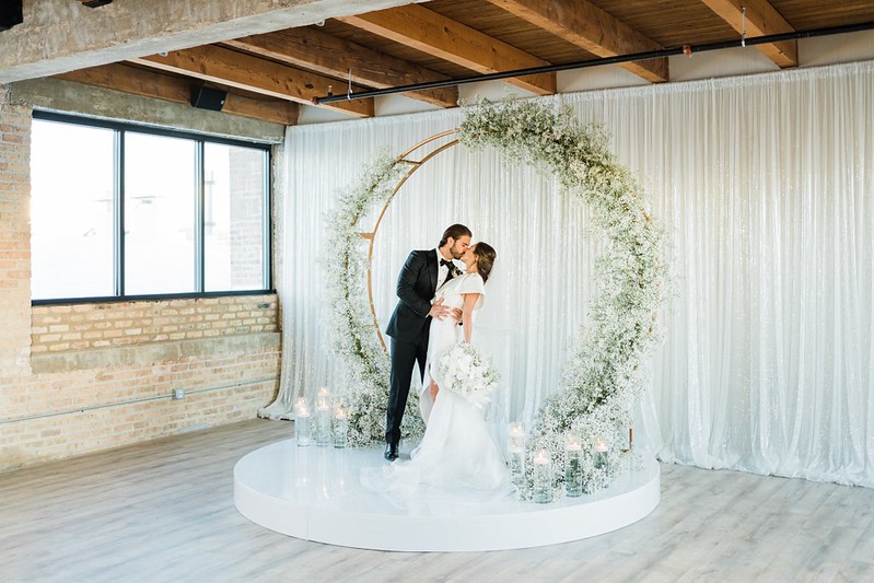 Groom And Bride Shared A Kiss, White Drape And Circled Greenery As Their Backdrop