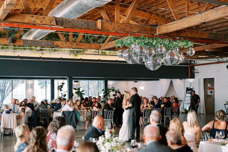 Newlyweds And Their Guests Celebrating Under The Hanging Mirror Balls With Greenery