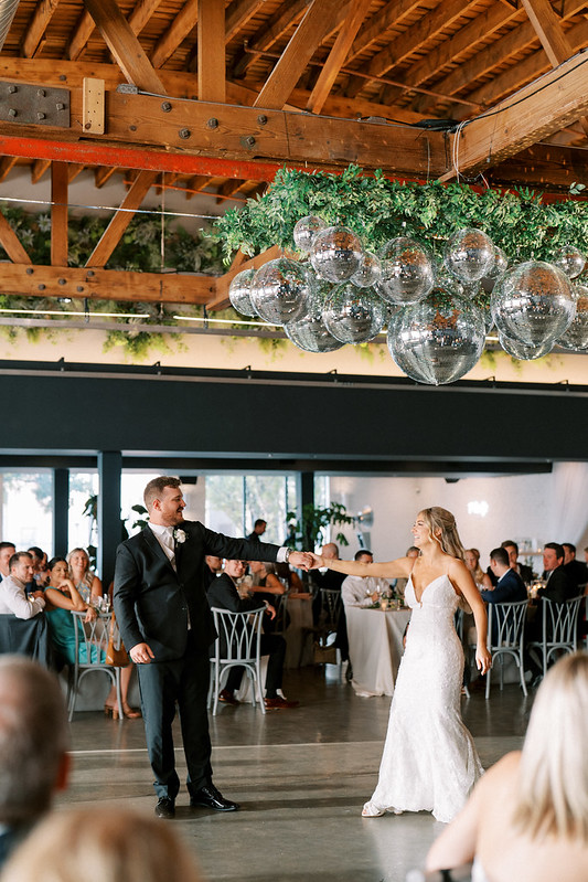Bride And Groom Dancing Under The Cluster Of Mirror Balls At Walden Chicago, Their Guests Are Watching Them.