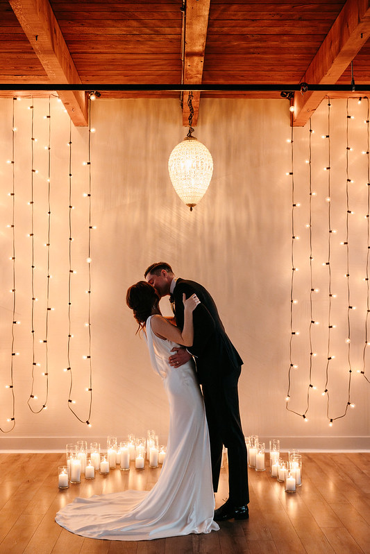 Bride And Groom Shared A Kiss Under The Acorn Chandelier And String Lights At Their Ceremony