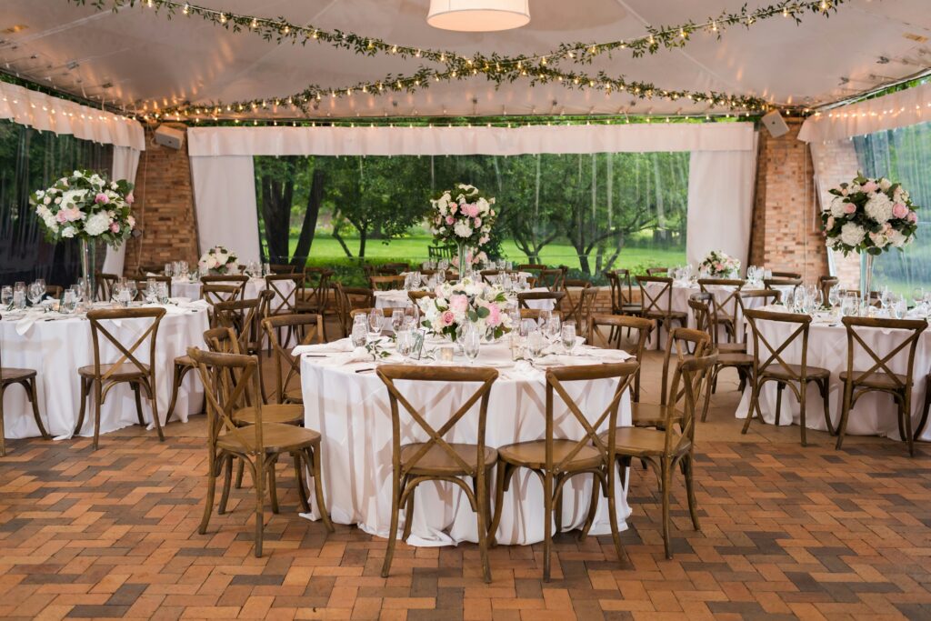 Reception With Hanging String Lights And Greenery, Wooden Chairs And White Tablecloths
