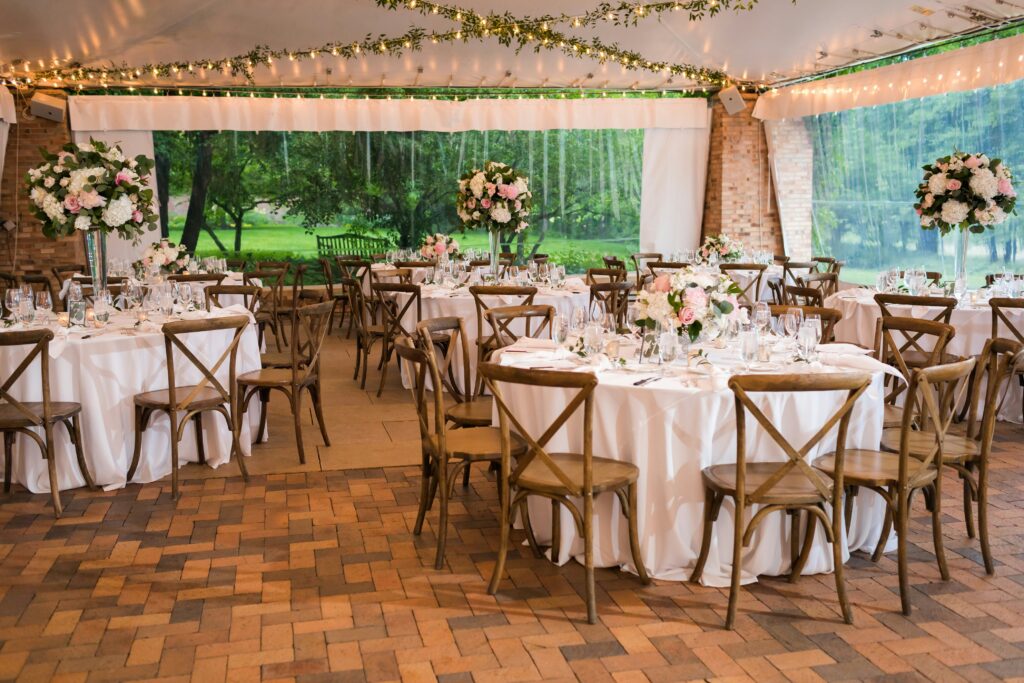 Reception With Hanging String Lights And Greenery, Wooden Chairs And White Tablecloths